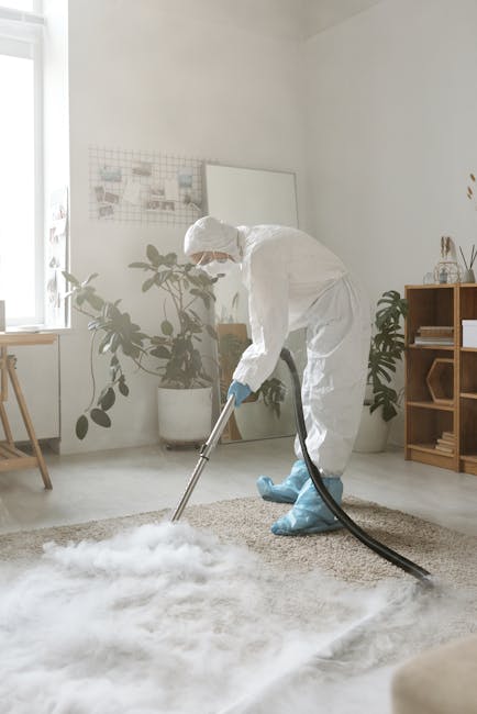 A person holding a yellow portable carpet cleaner with a black vent, positioned over an ornate, patterned area rug in a room with wooden flooring. The individual appears to be preparing for surface cl