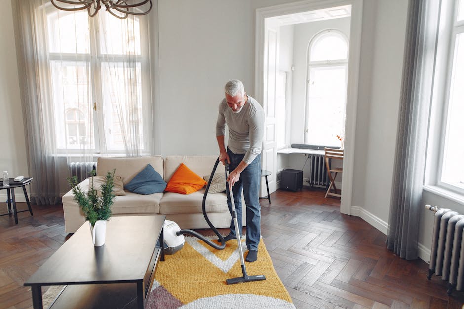 Close-up view of a person operating a yellow portable carpet cleaning machine, with hands firmly gripping the device while pressing a button on the handle. The machine is positioned on a patterned, mu