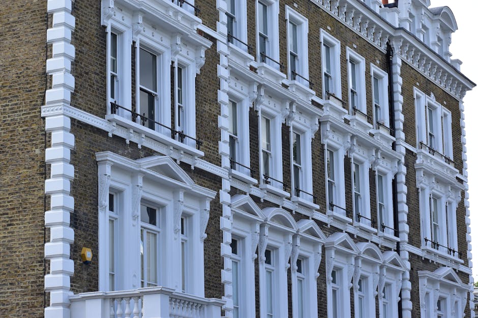 A black-and-white photograph of Warwick Avenue in Maida Vale, showing a narrow city street lined with multi-story Victorian-style buildings featuring decorative facades and large windows. The street s